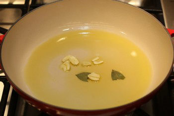 garlic and bay leaf cooking in olive oil in a pan on top of stove