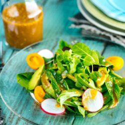spring mix salad featuring avocado, heirloom tomatoes, radishes on a plate