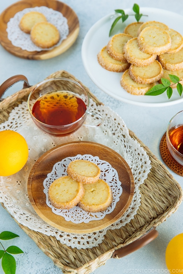 A wooden plate containing Meyer Lemon Sables and a cake stand behind holding more sables.