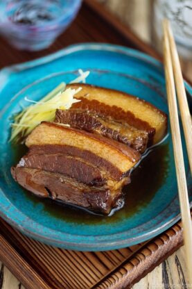 A blue plate containing 2 slices of Rafute (Okinawan Braised Pork Belly) garnished with julienned ginger.