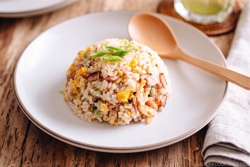 Japanese fried rice with egg, ham, and green onion on a white plate.