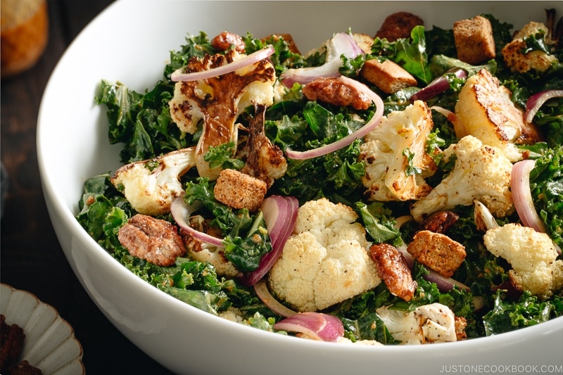 A large white bowl containing Roasted Cauliflower Kale Salad tossed with Miso Tahini Dressing.