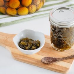 Plum jam in a white small bowl. Plum jam in a jar and plum wine in the back.
