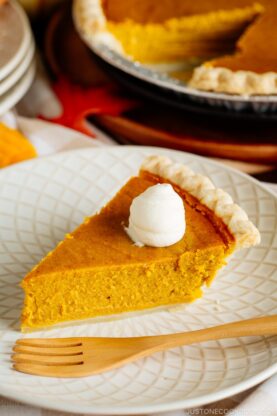 White plate containing a slice of Kabocha Pie topped with freshly whipped cream.