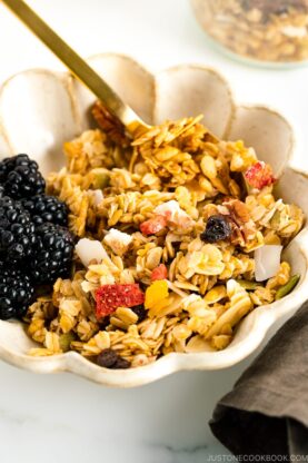 A white bowl containing homemade granola with blackberries.