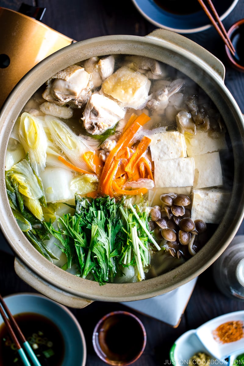 A Japanese earthenware pot (donabe) containing Mizutaki (Japanese Chicken Hot Pot) filled with chicken, tofu, mushrooms, and all kinds of vegetables.