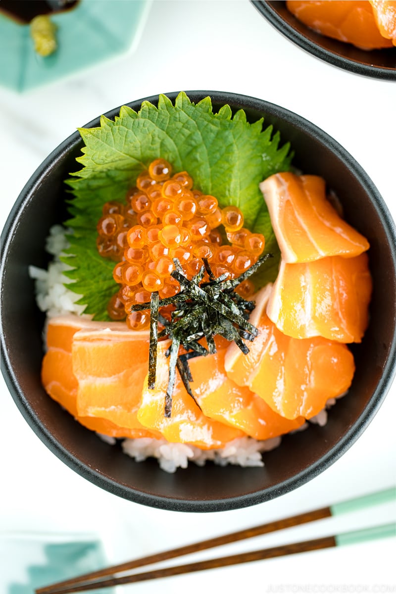 A black bowl containing a bed of rice topped with sashimi grade salmon, ikura, and shredded nori.