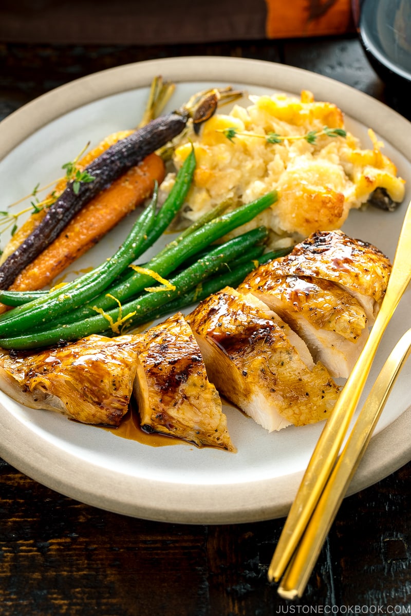 A ceramic dish containing Honey Soy Glazed Spatchcock Chicken, green beans, carrots, and macaroni gratin.
