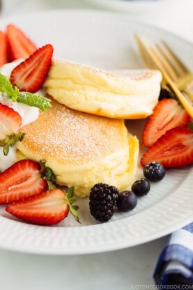 A white plate containing fluffy Japanese soufflé pancakes and berries.