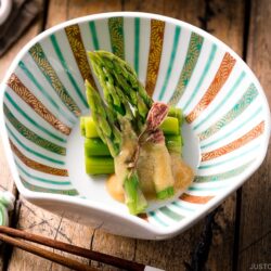 A shell shaped bowl containing Asparagus with Miso Dressing (Karashi Sumisoae) garnished with salt pickled cherry blossom.