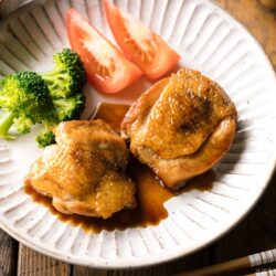 A plate containing butter shoyu chicken, broccoli, and tomatoes.
