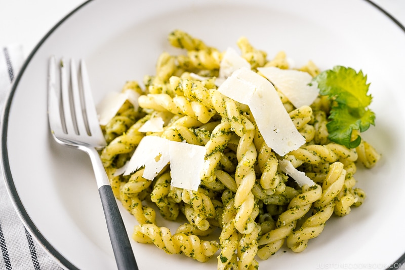 A white bowl containing Shiso Pesto Pasta garnished with shaved Parmesan cheese and shiso leaves.