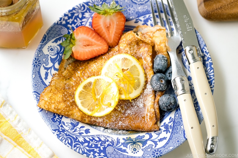 A blue plate containing lemon and sugar crepe along with fresh berries.