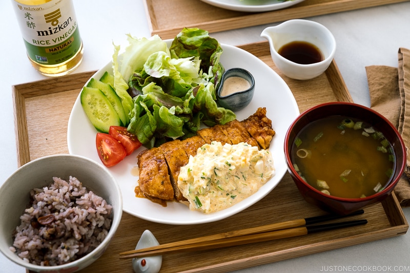A white plate containing crispy chicken dressed with a tangy sauce and served with homemade tartar sauce.