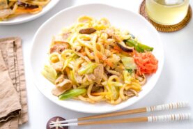 A white round plate containing Yaki Udon (Japanese Stir-Fried Udon Noodles) garnished with red pickled ginger.