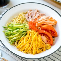 A white plate containing cold ramen (Hiyashi Chuka) with julienned cucumber, ham, egg, and more!