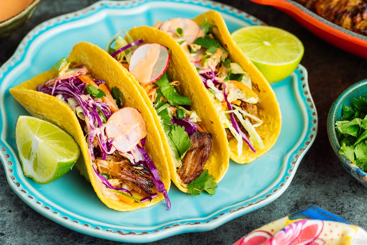 The wooden table with bowls and plates containing Asian Pulled Pork Taco ingredients.