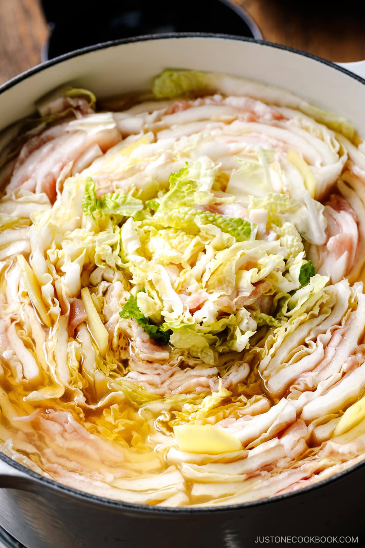 A Le Creuset pot containing Mille-Feuille Nabe, which is a hot pot dish with layers of pork belly slices and napa cabbage slices in a dashi broth.