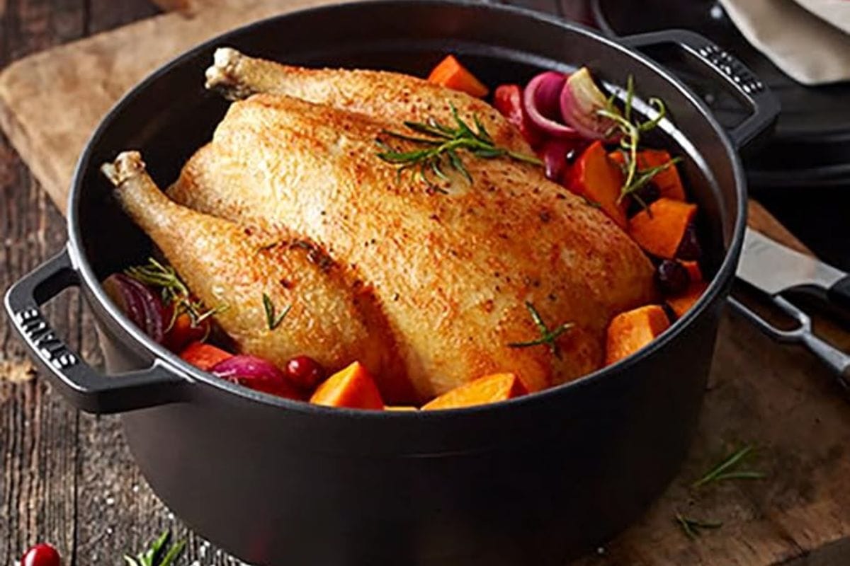 Juicy roasted chicken with vegetables in a black Dutch oven, garnished with fresh herbs, on a rustic wooden surface, perfect for Japanese-inspired home cooking and meal prep.