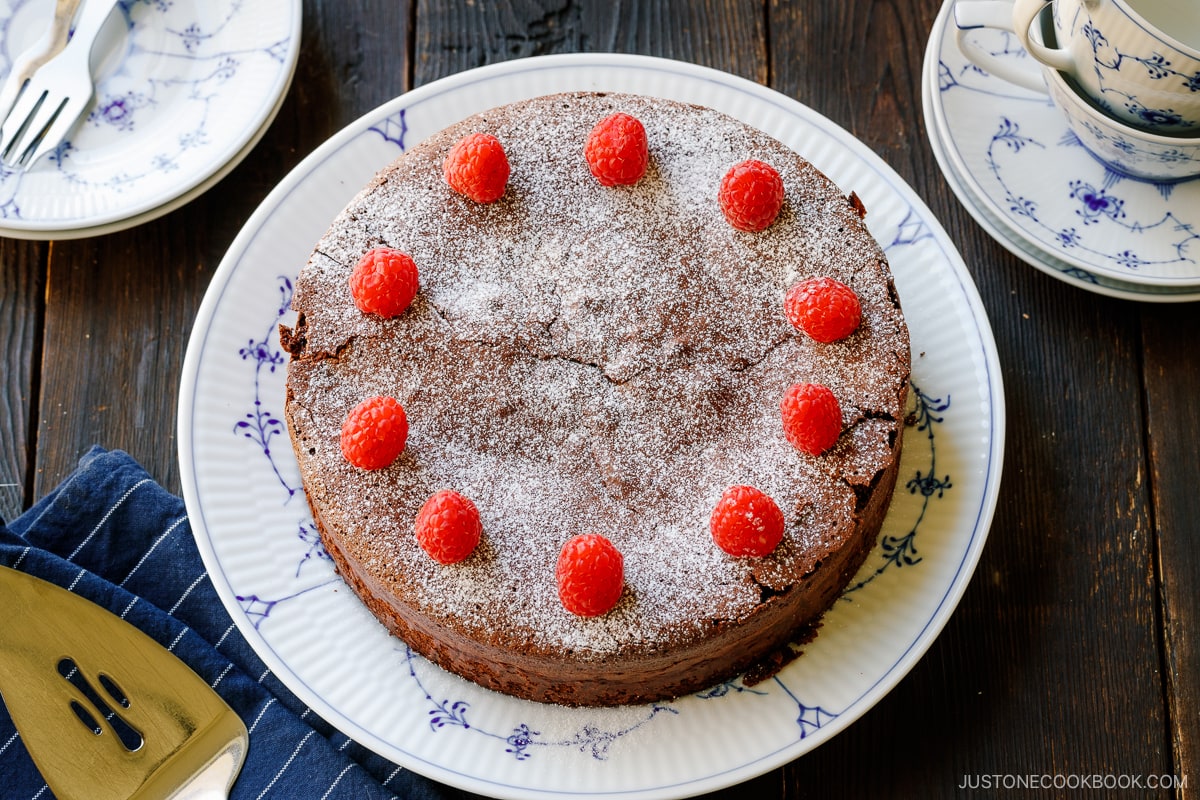 A large plate containing Chocolate Gateau (Chocolate Cake) dusted with powdered sugar and decorated with raspberries.