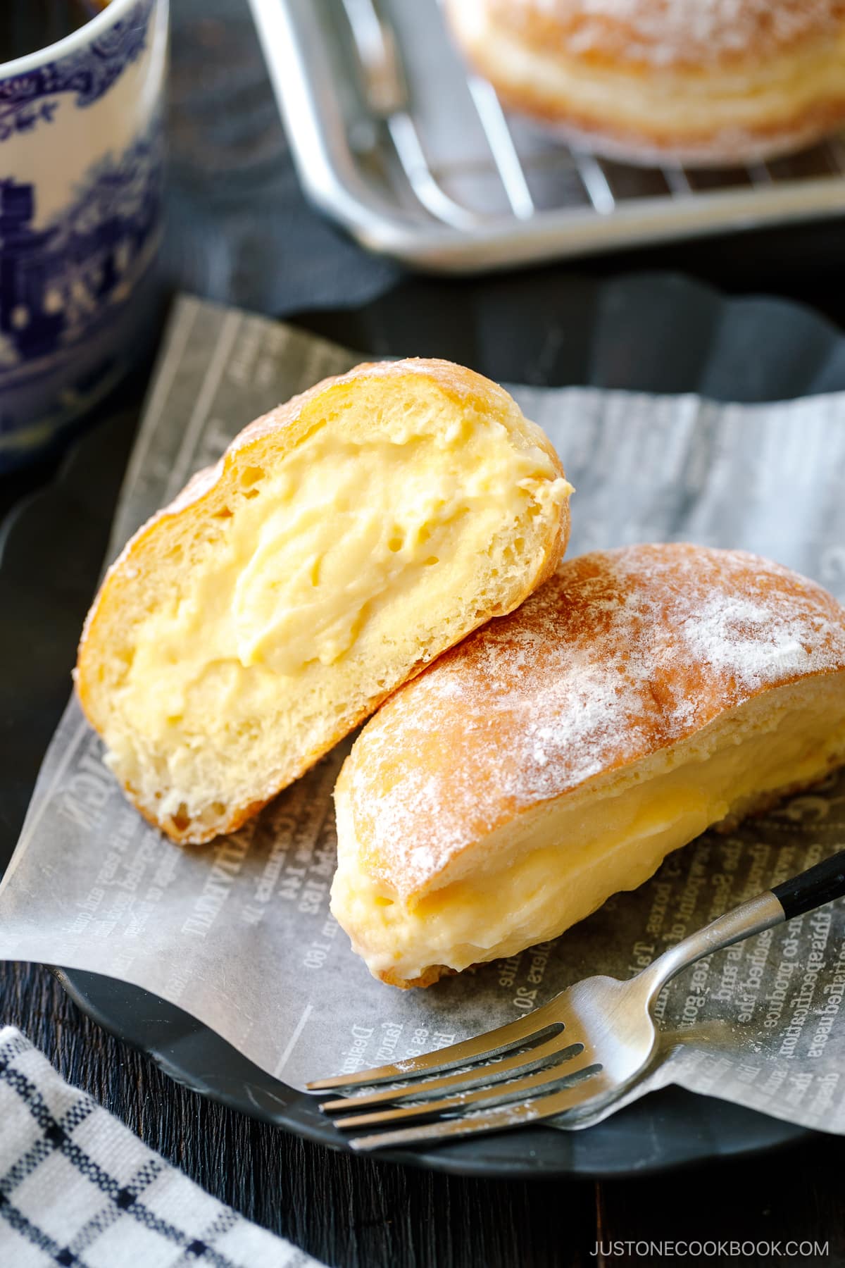 A black fluted plate containing Nama Donuts dusted with powdered sugar and filled with the custard.