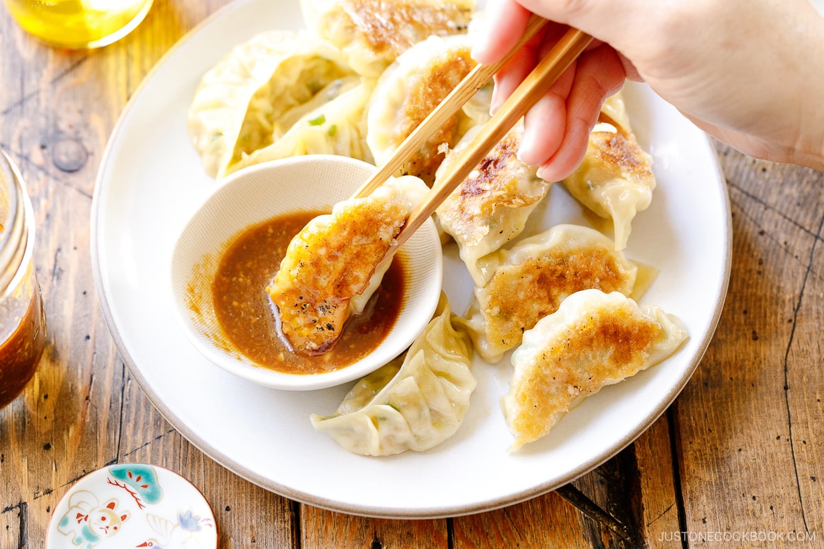 A round plate containing Japanese pan-fried dumplings, Napa Cabbage Gyoza, served with a savory miso dumpling sauce.