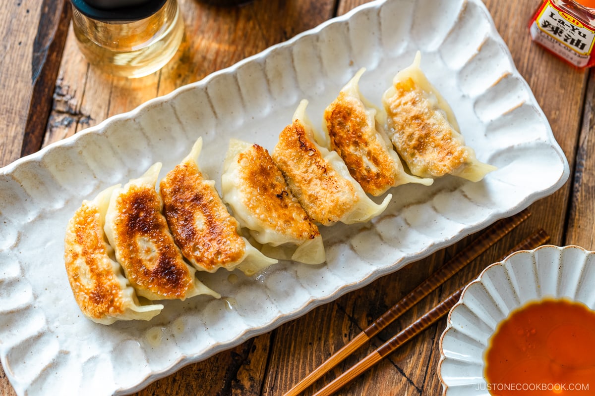 A rectangular plate containing gyoza (Japanese potstickers or pan-fried dumplings) with a small plate of dipping sauce made with soy sauce, vinegar, and Japanese chili oil.