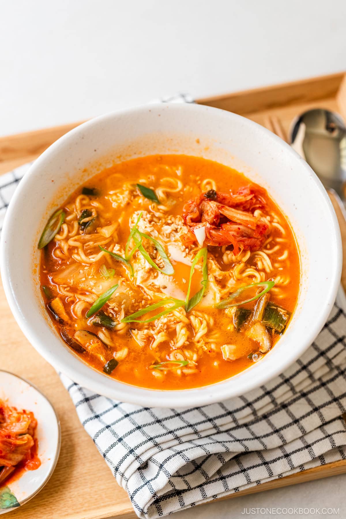 A white ramen bowl containing Korean ramen (ramyeon), topped with soft-cooked egg, kimchi, and green onions.