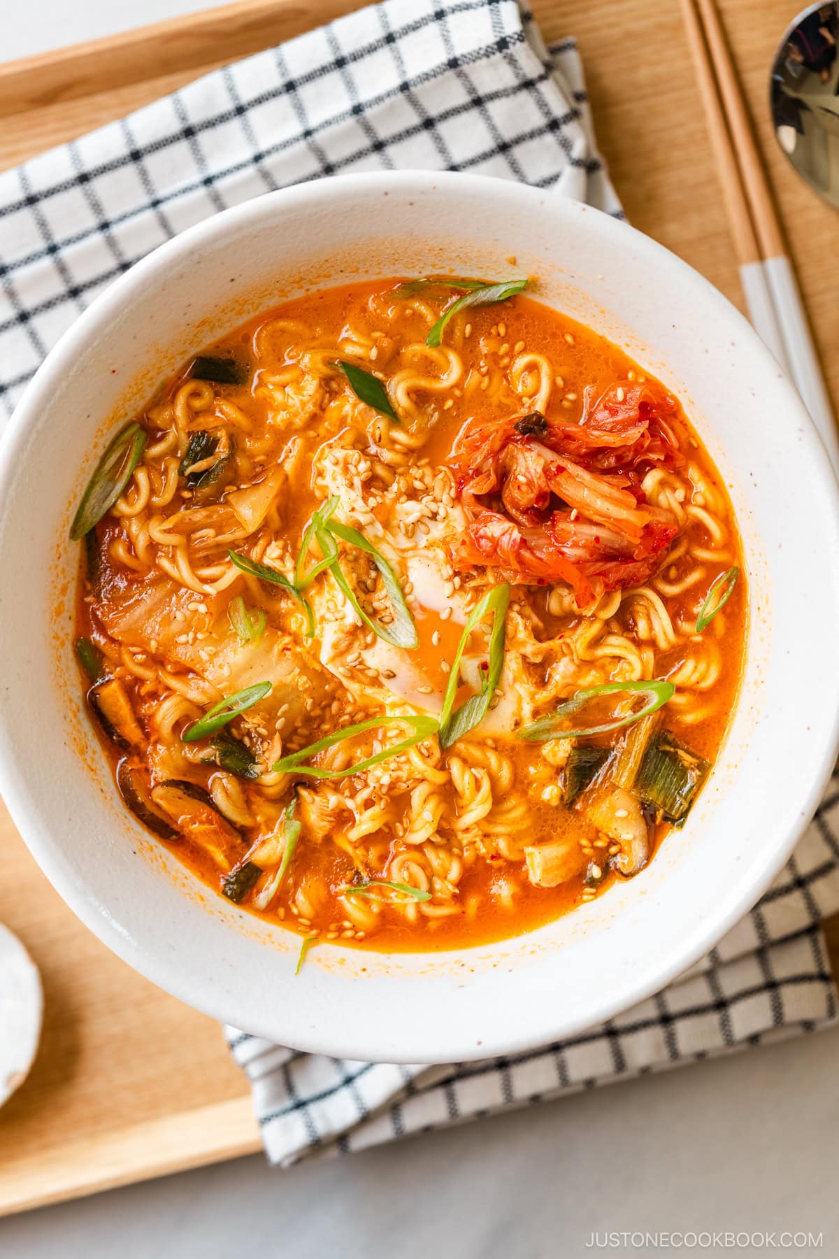 A white ramen bowl containing Korean ramen (ramyeon), topped with soft-cooked egg, kimchi, and green onions.