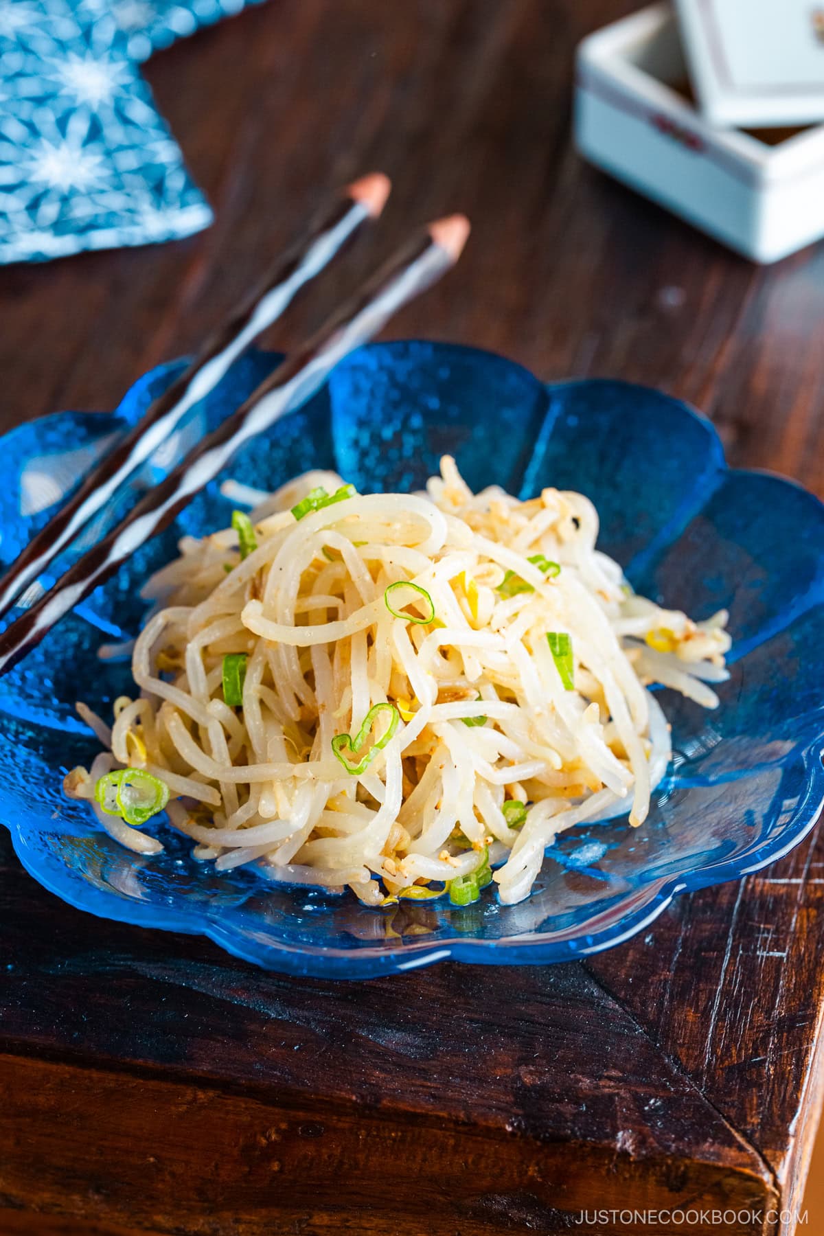 A blue plate containing Bean Sprout Salad, seasoned with sesame oil and mixed with (ground) sesame seeds and green onions.