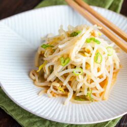 A white plate containing Bean Sprout Salad, seasoned with sesame oil and mixed with (ground) sesame seeds and green onions.