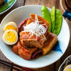 A bowl containing Kakuni, Japanese braised pork belly, served with julienned white scallion, boiled egg, and karashi mustard.