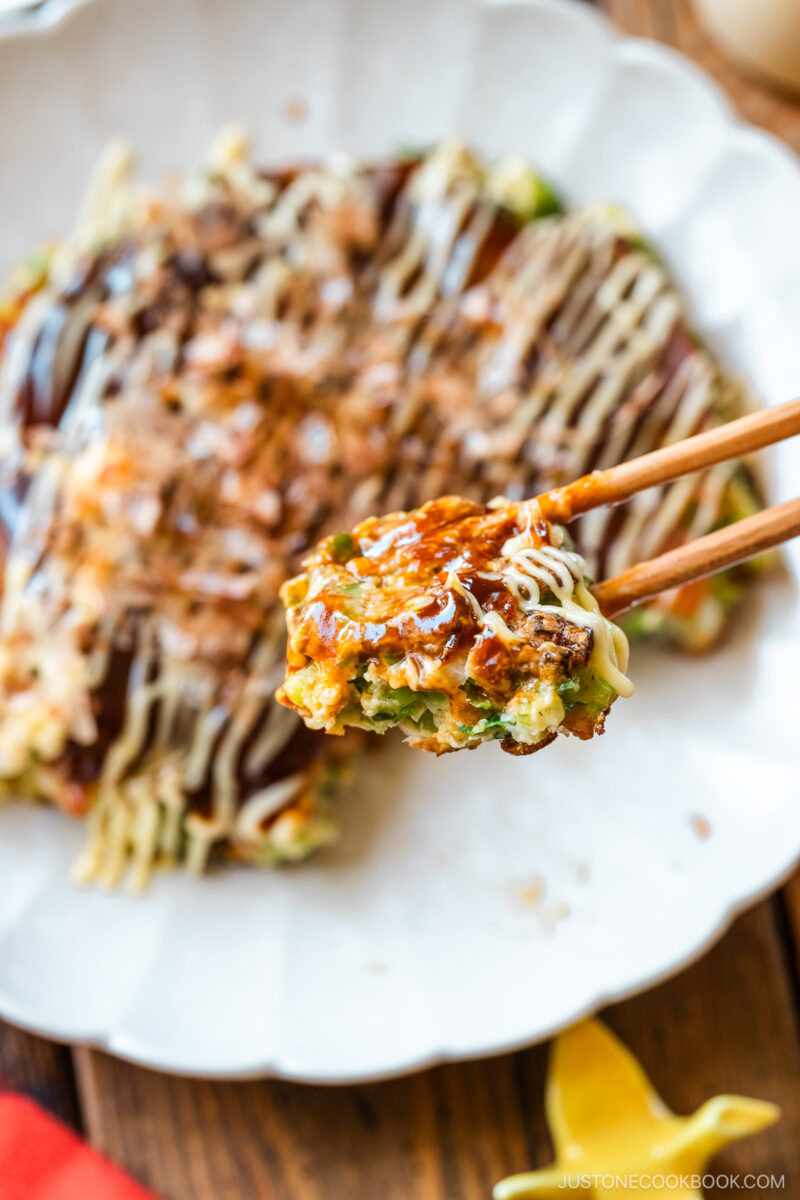 Chopsticks picking up a bite of negiyaki, Japanese scallion okonomiyaki.