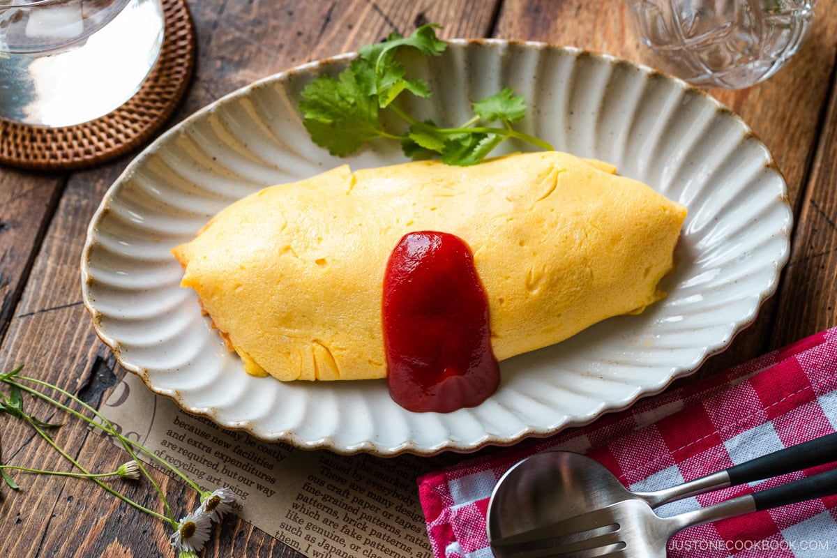 An oval plate containing Omurice (Japanese Omelette Rice) drizzled with Japanese ketchup.