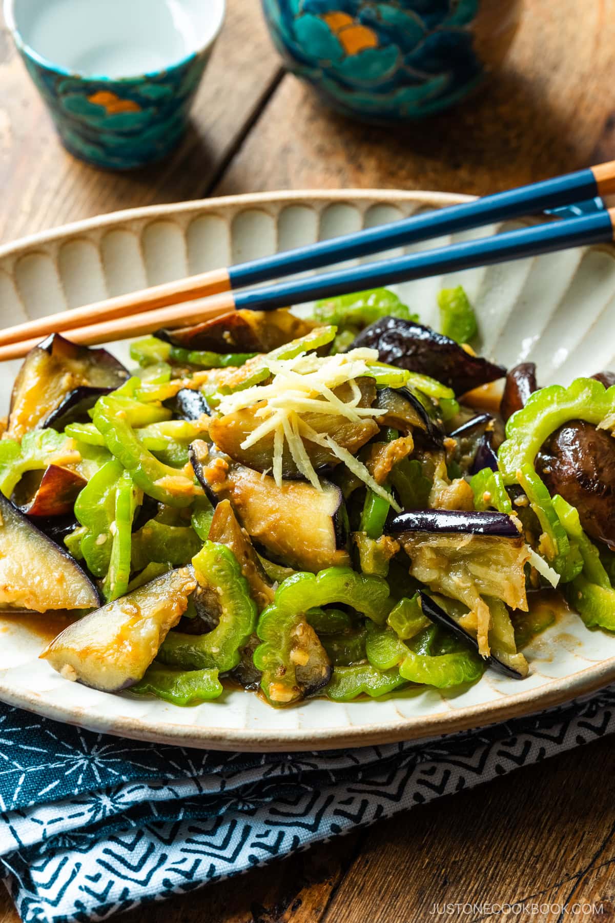 An oval fluted plate containing Stir-Fried Bitter Melon and Eggplant topped with julienned ginger.