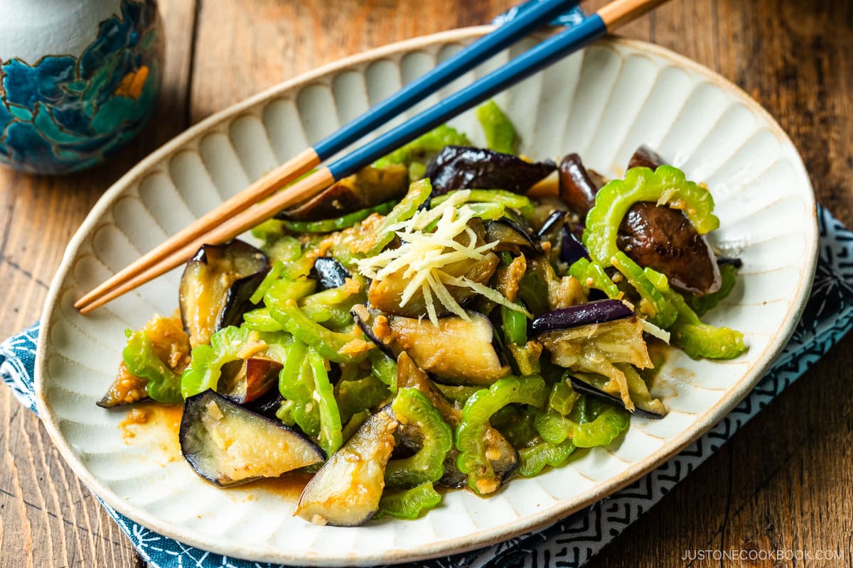 An oval fluted plate containing Stir-Fried Bitter Melon and Eggplant topped with julienned ginger.