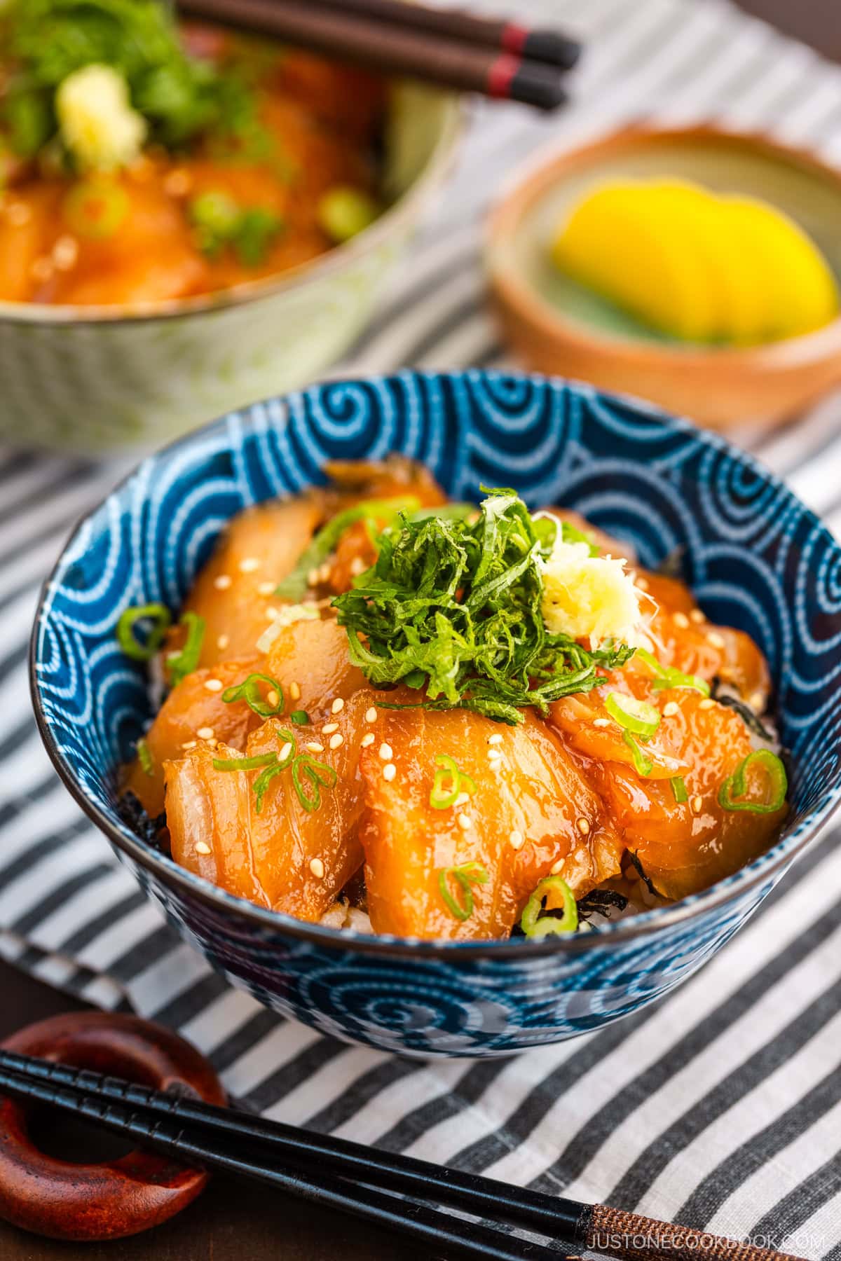 A blue bowl containing soy sauce marinated albacore tuna over steamed rice, topped with shiso and grated ginger.