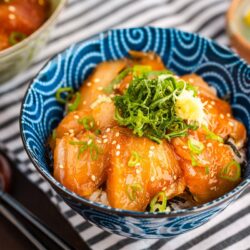 A blue bowl containing soy sauce marinated albacore tuna over steamed rice, topped with shiso and grated ginger.