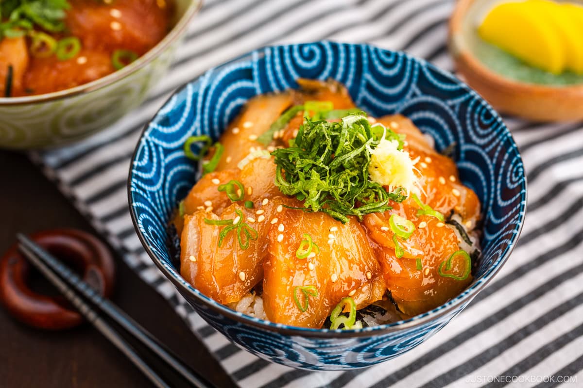 A blue bowl containing soy sauce marinated albacore tuna over steamed rice, topped with shiso and grated ginger.