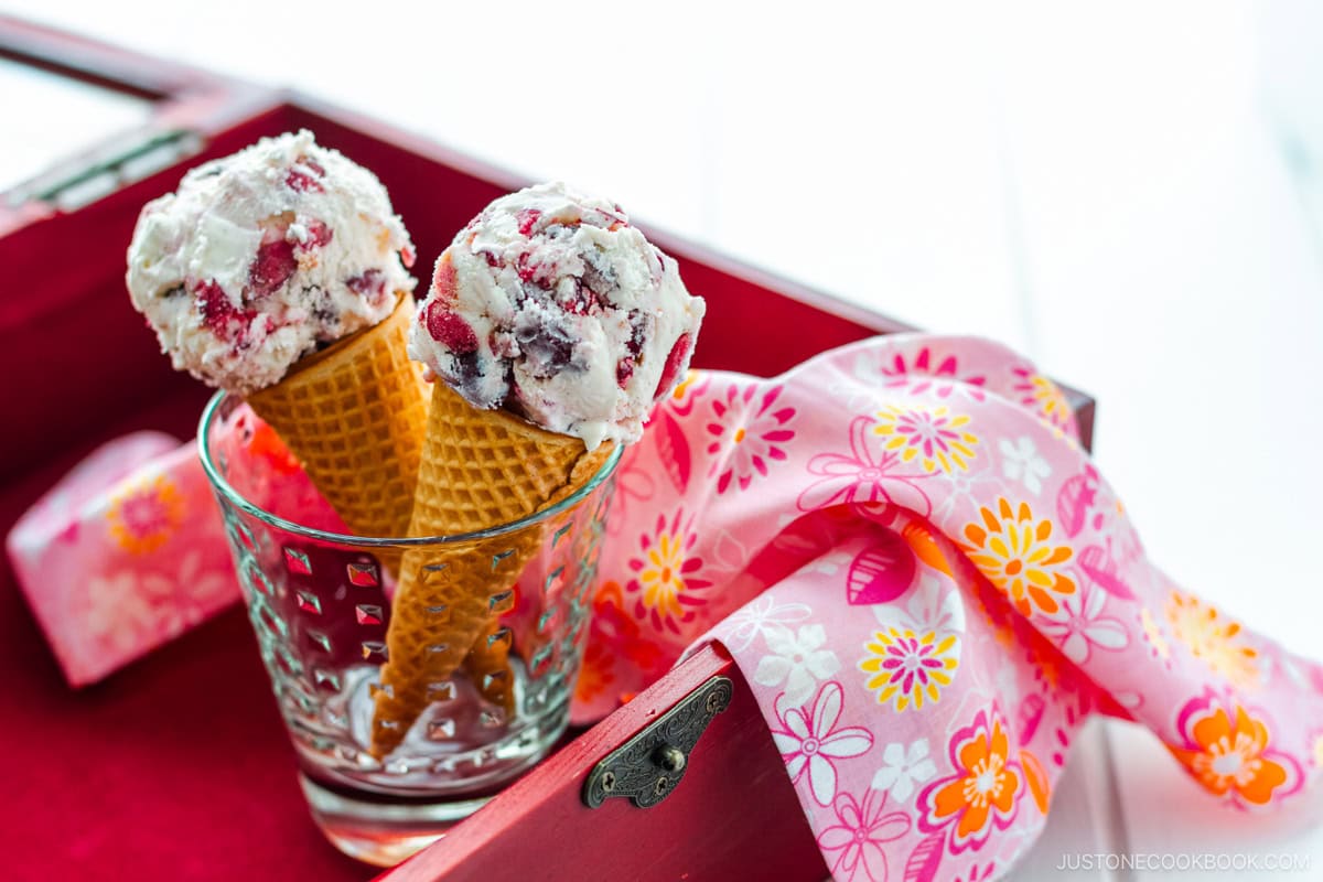 A glass cup containing cherry ice cream on a waffle cone.