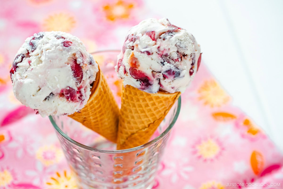 A glass cup containing cherry ice cream on a waffle cone.