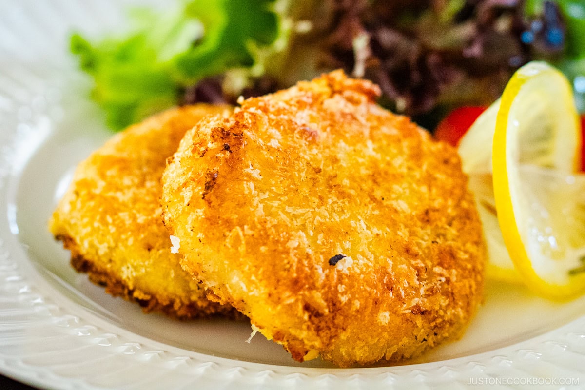 A white plate containing creamy crab croquettes, served with salad and a slice of lemon.