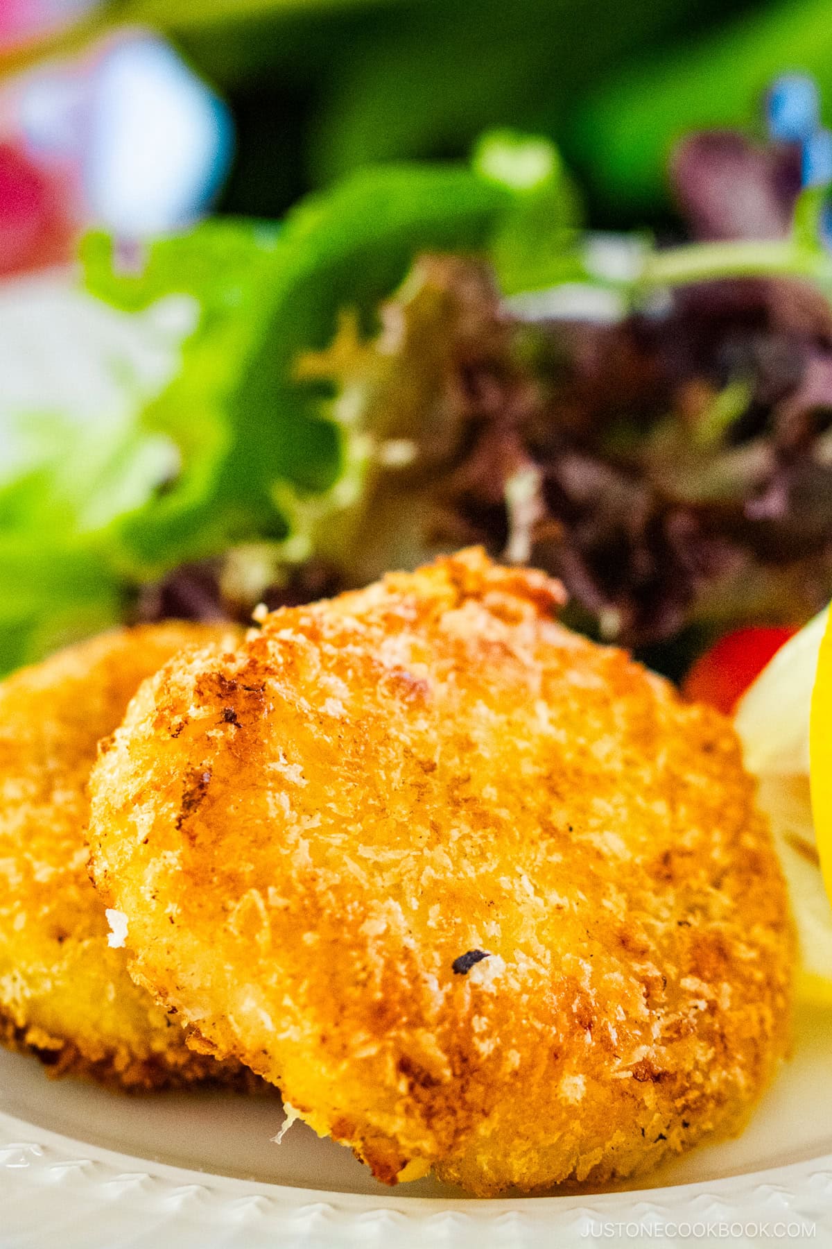 A white plate containing creamy crab croquettes, served with salad and a slice of lemon.