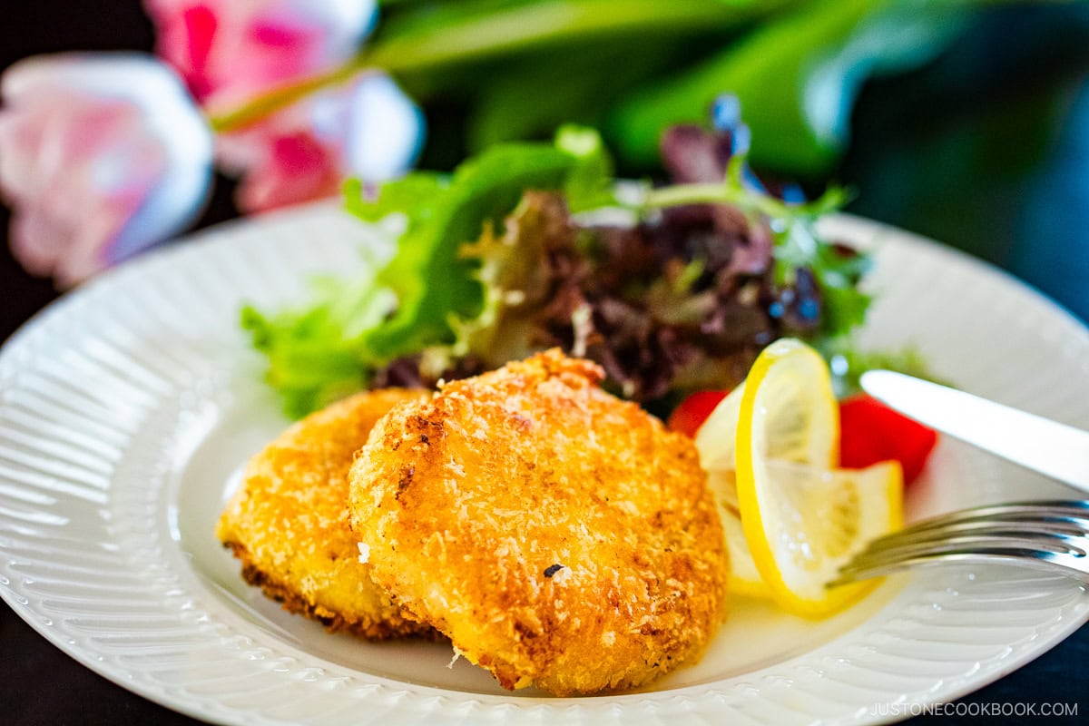 A white plate containing creamy crab croquettes, served with salad and a slice of lemon.