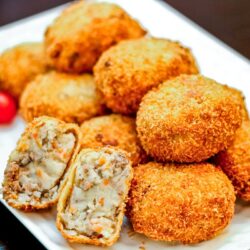A white rectangular plate containg potato and meat croquettes.