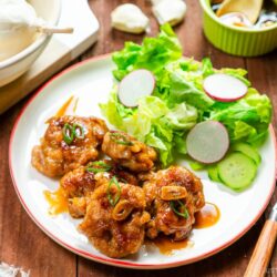 A white plate containing teriyaki pork balls and green salad.