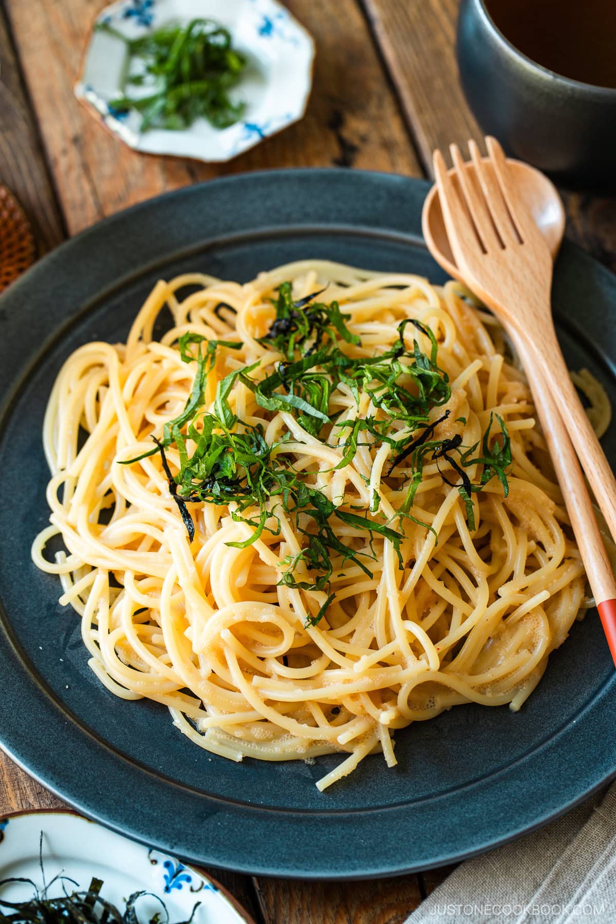 A black round plate containing metaiko pasta - Japanese spaghetti with spicy salted cod roe topped with julienned shiso and shredded nori seaweed.