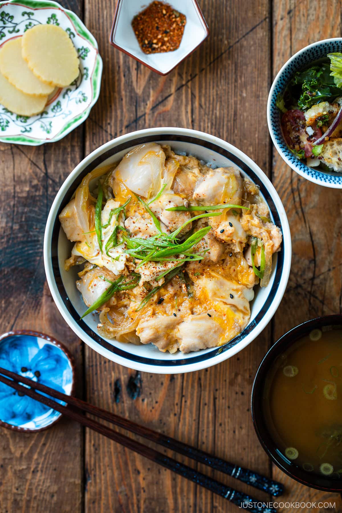 A Japanese ceramic bowl containing Oyakodon, a chicken and egg rice bowl dish garnish with green onion.
