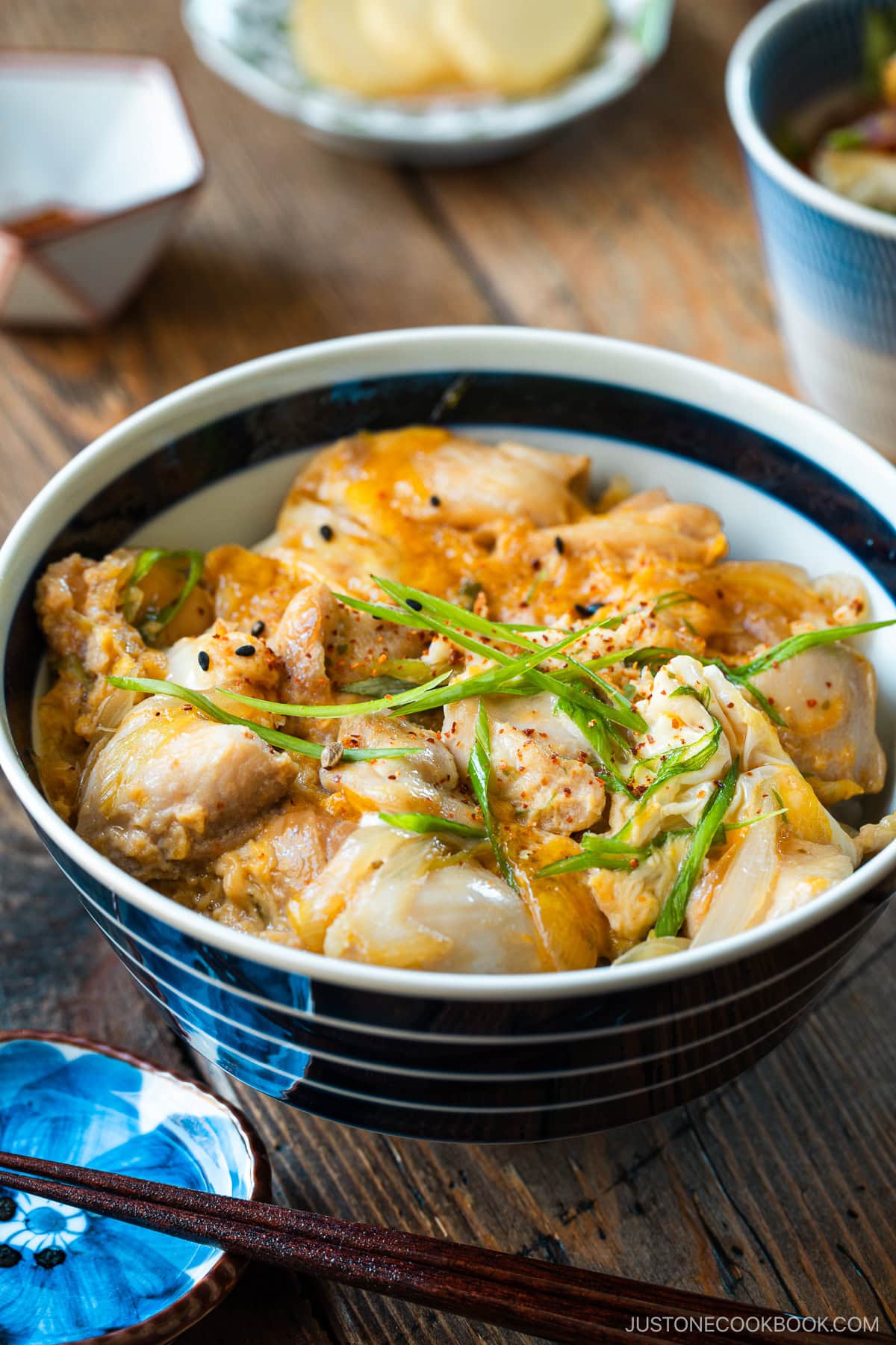 A Japanese ceramic bowl containing Oyakodon, a chicken and egg rice bowl dish garnish with green onion.