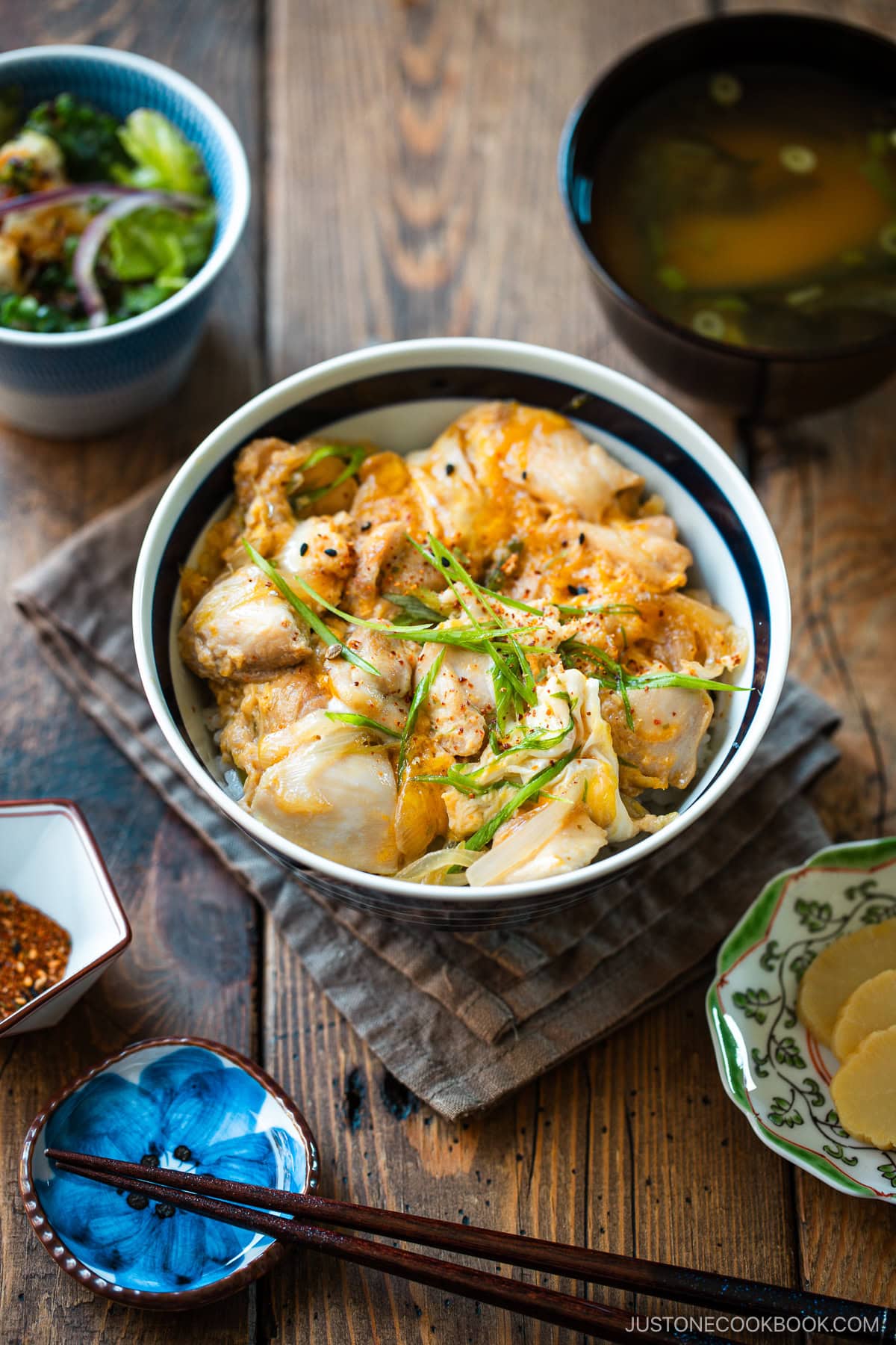 A Japanese ceramic bowl containing Oyakodon, a chicken and egg rice bowl dish garnish with green onion.
